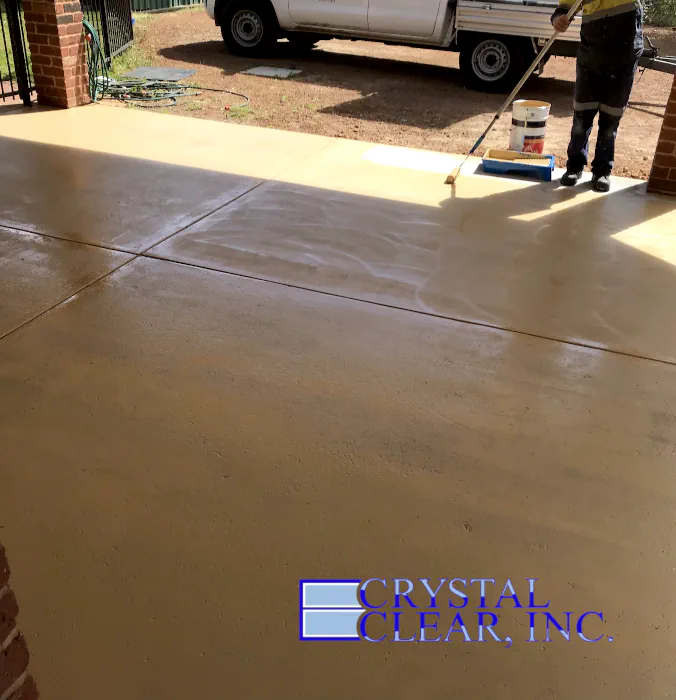 an image of a man of color applying a Epoxy Garage Floor, its an ultra clear coat, the garage door is open and the sunny summer day makes the floor look great, shiny and clear.
