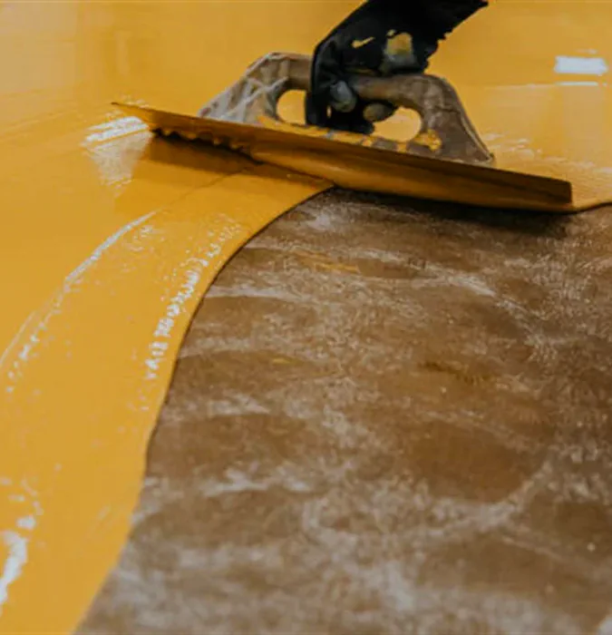 an image of a Epoxy Finish Garage Floor installation, the epozy is a bright yellow and its being troweled around the grey cement floor