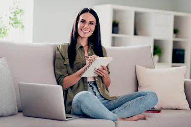 a 3rd image of a Middle Aged Latino Woman Smiling looking at a notepad while she is writing down design ideas for her home's basement, garage, and patio areas, she look very happy sitting on a couch in blue jeans and a loose fitting dark green button up shirt